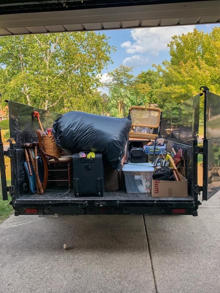 Pickup truck bed loaded with assorted moving boxes, bags, and household items in a driveway