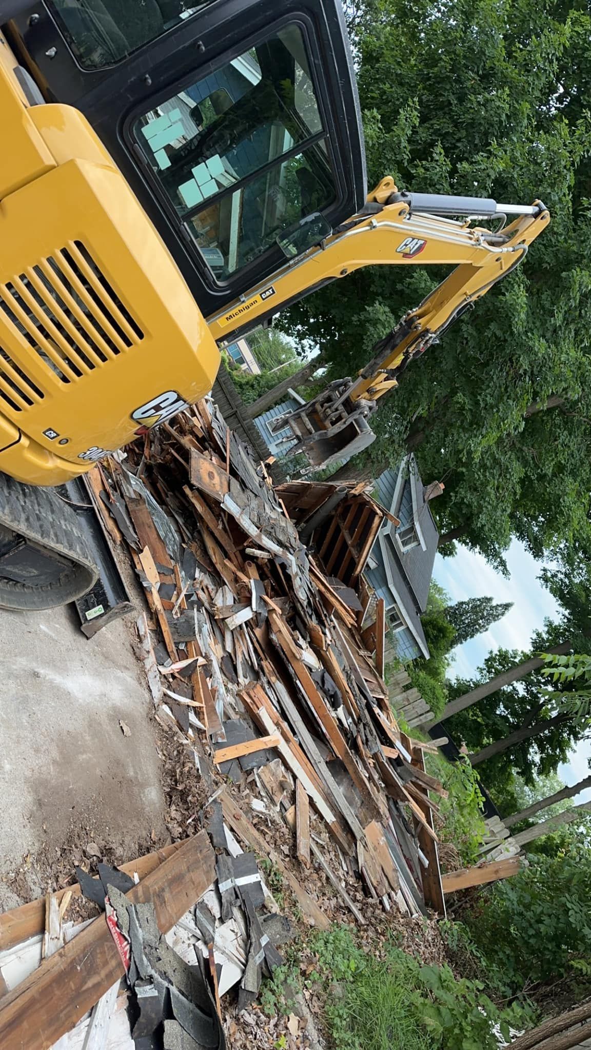 Yellow excavator demolishing a collapsed structure amid rubble and trees