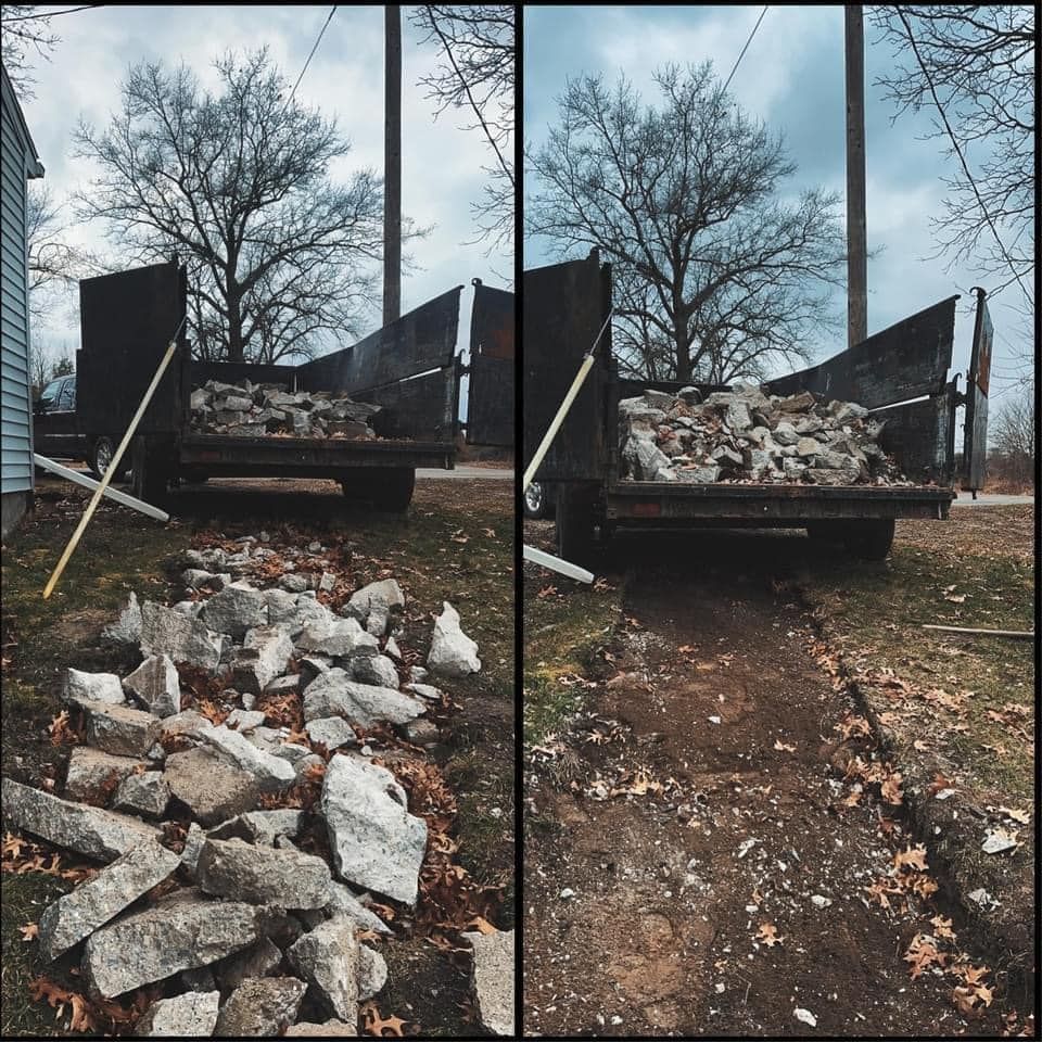 Dump truck unloading broken concrete onto a dirt road beside a leafless tree