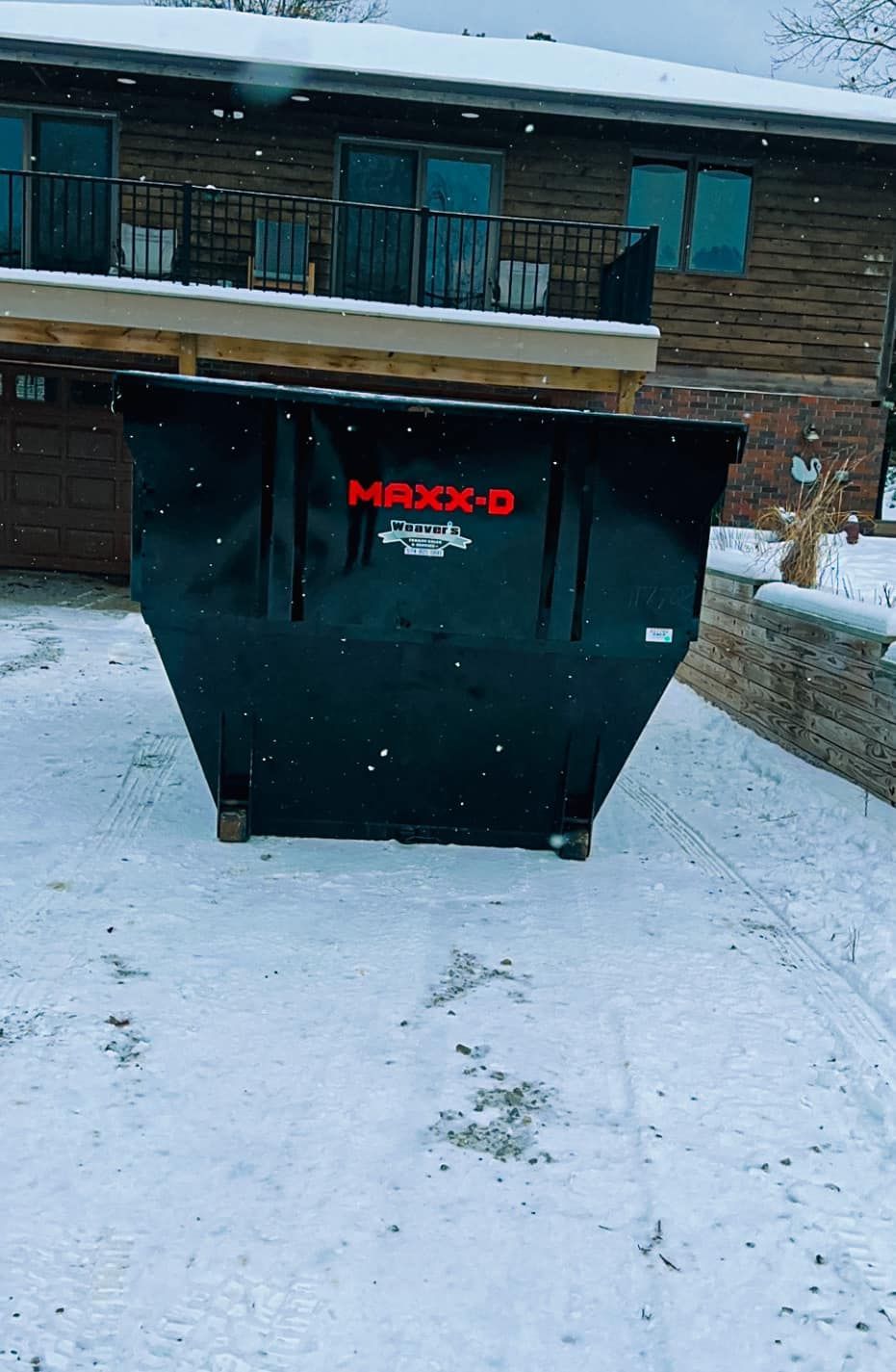 Black dumpster in snowy apartment complex courtyard beside a brick building.