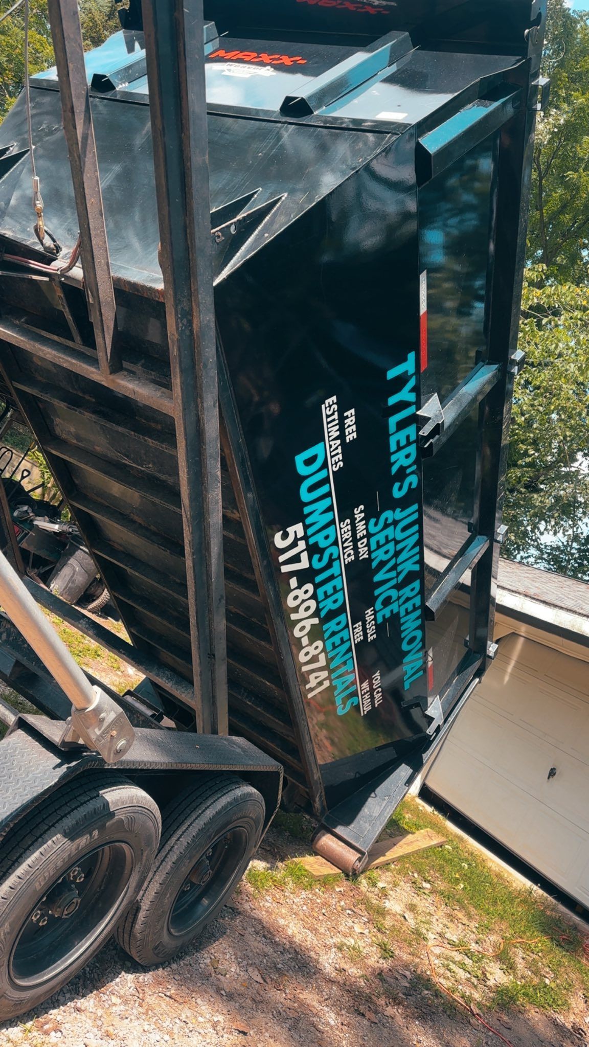 Overturned trailer with black sides and turquoise lettering beside a driveway and trees.
