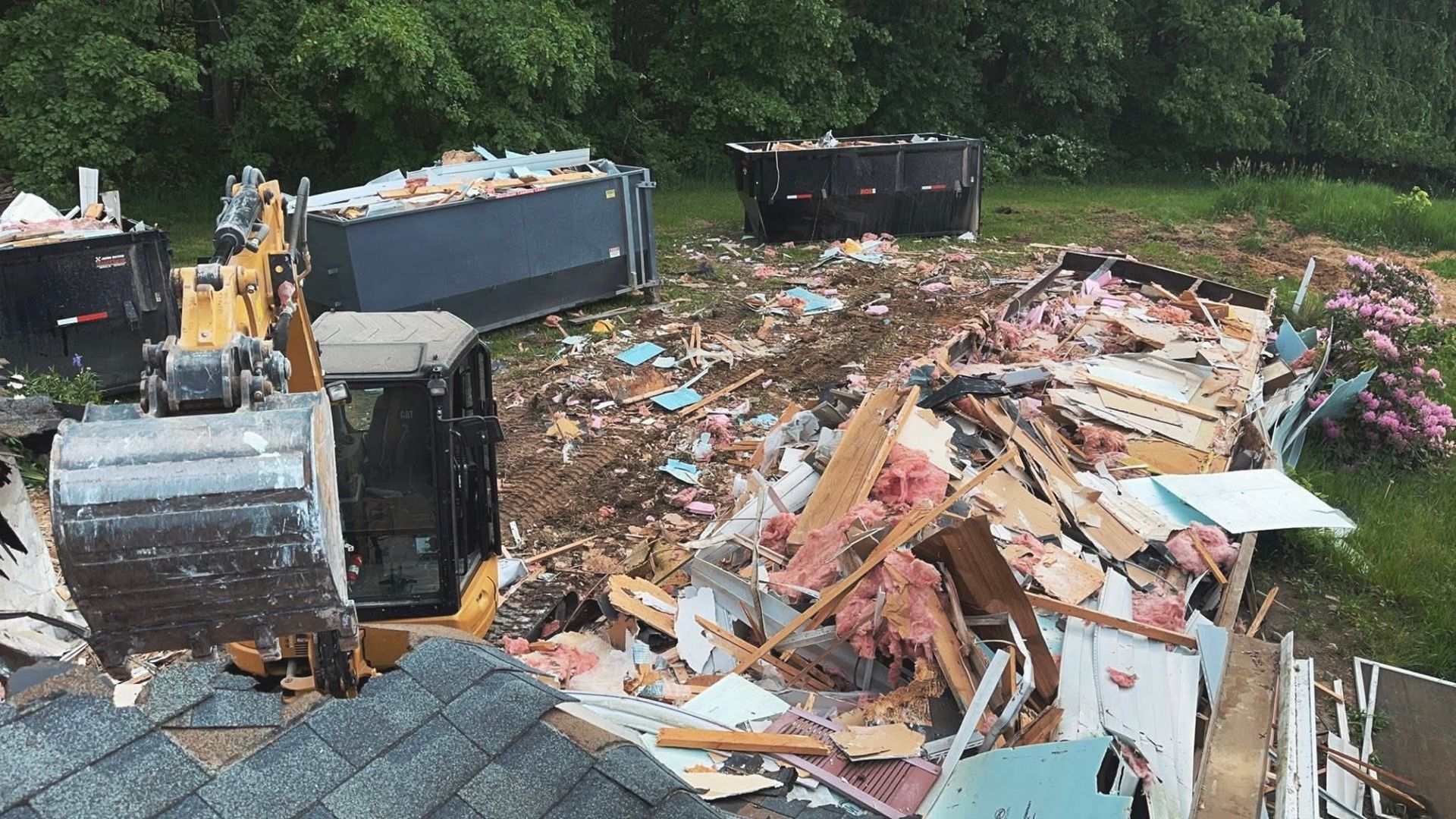 Overturned dumpster beside a large pile of construction debris in a wooded area