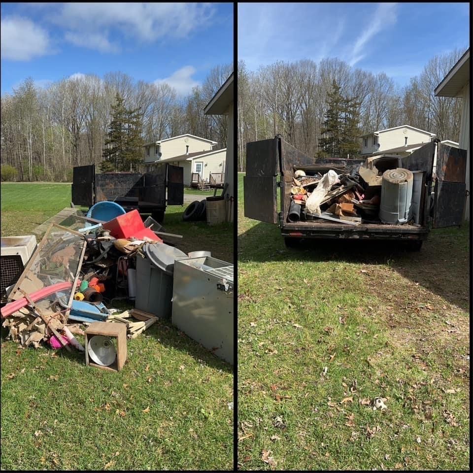 Yard debris and furniture piled on a trailer in a grassy yard beside a house on a sunny day