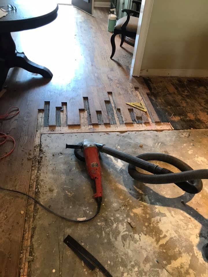 Hardwood floor removal in progress with power tool and vacuum. Sections of floor missing.