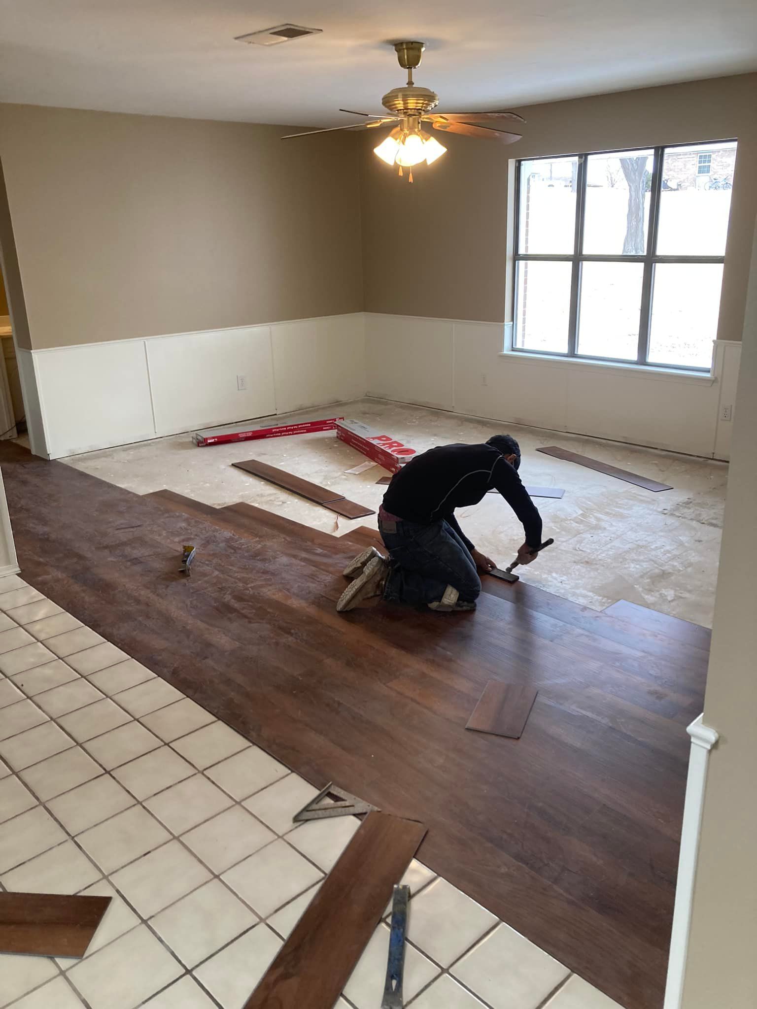 Person installing wood-look flooring in a room with beige walls and a large window.