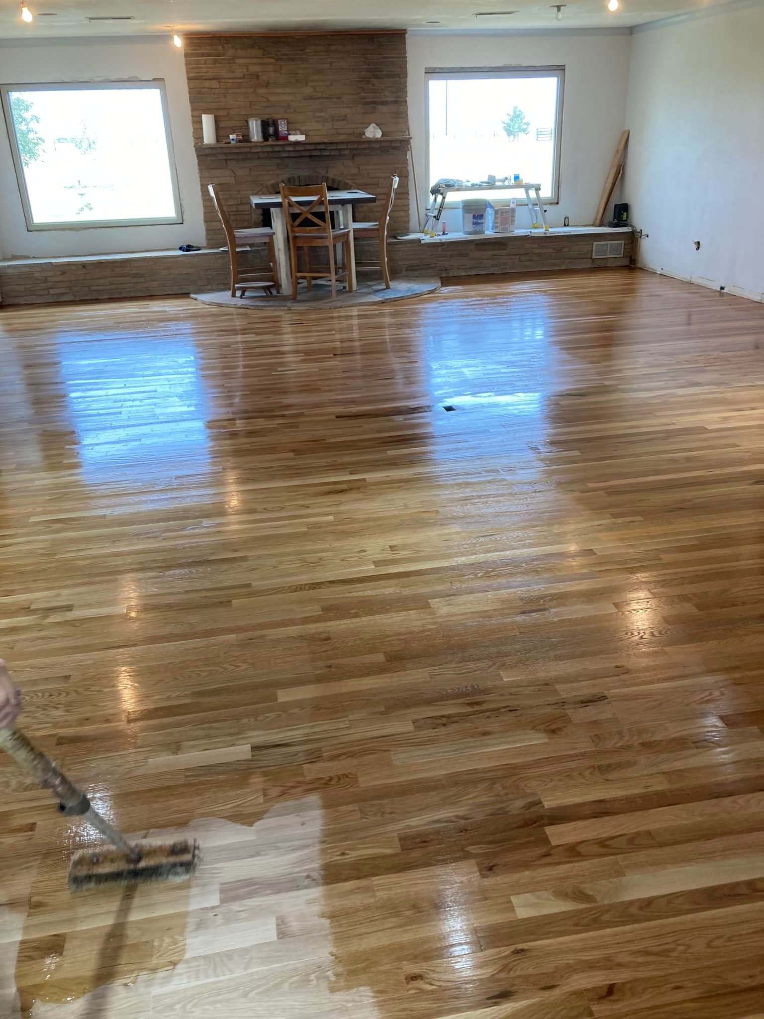 Wooden floor being finished with a liquid coating, indoors near windows and a fireplace.