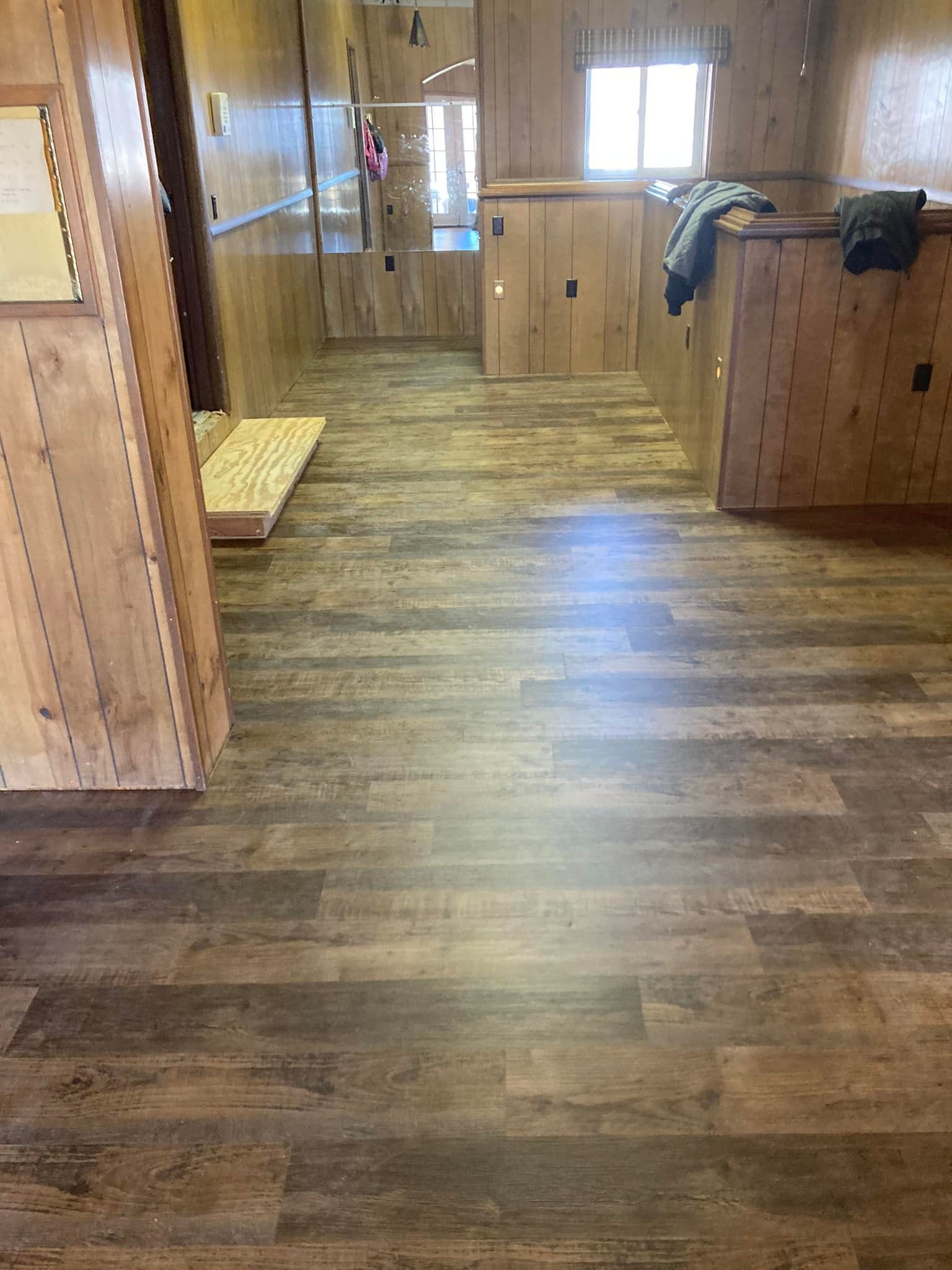 Interior of a trailer with wood paneling and wood-look flooring. Light streams through a window at the end.