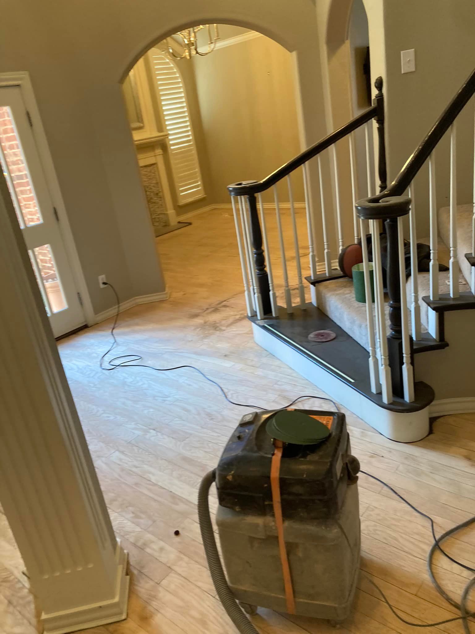 Hardwood floor being refinished. A sanding machine sits on the floor near a staircase.