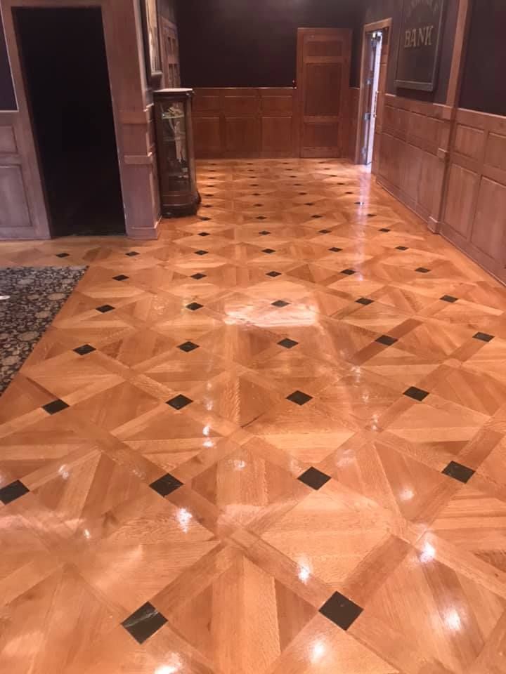Wooden floor with geometric pattern, black squares, and glossy finish in a hallway with dark walls and wood paneling.