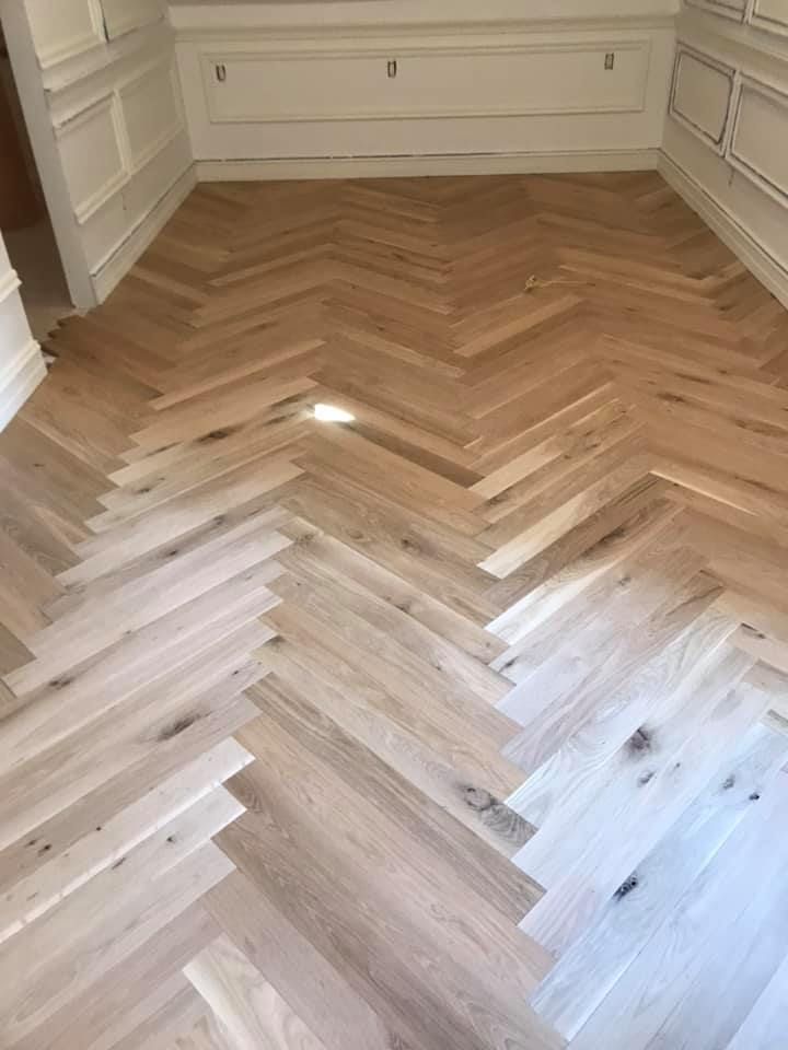 Herringbone pattern hardwood floor in a room with white wainscoting and molding.