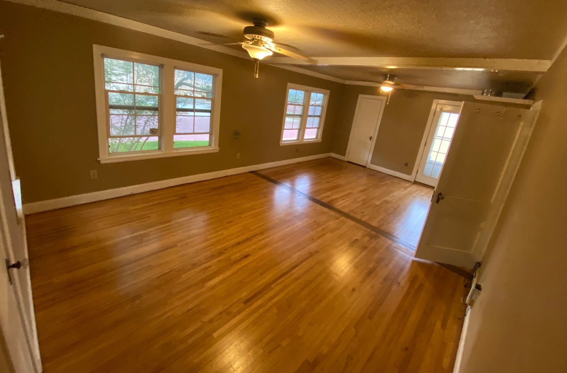 Empty room with hardwood floors, windows, two ceiling fans, and a door.