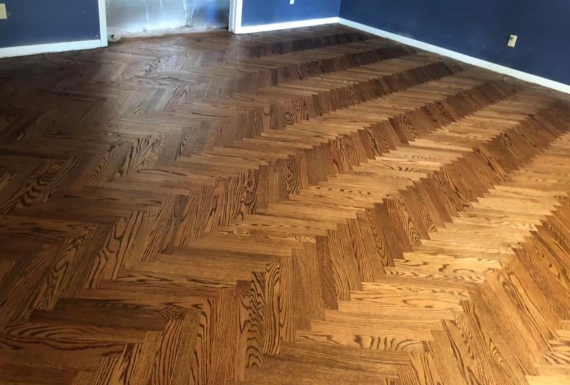 Diagonal pattern of reddish-brown wooden parquet flooring with blue walls and white trim.