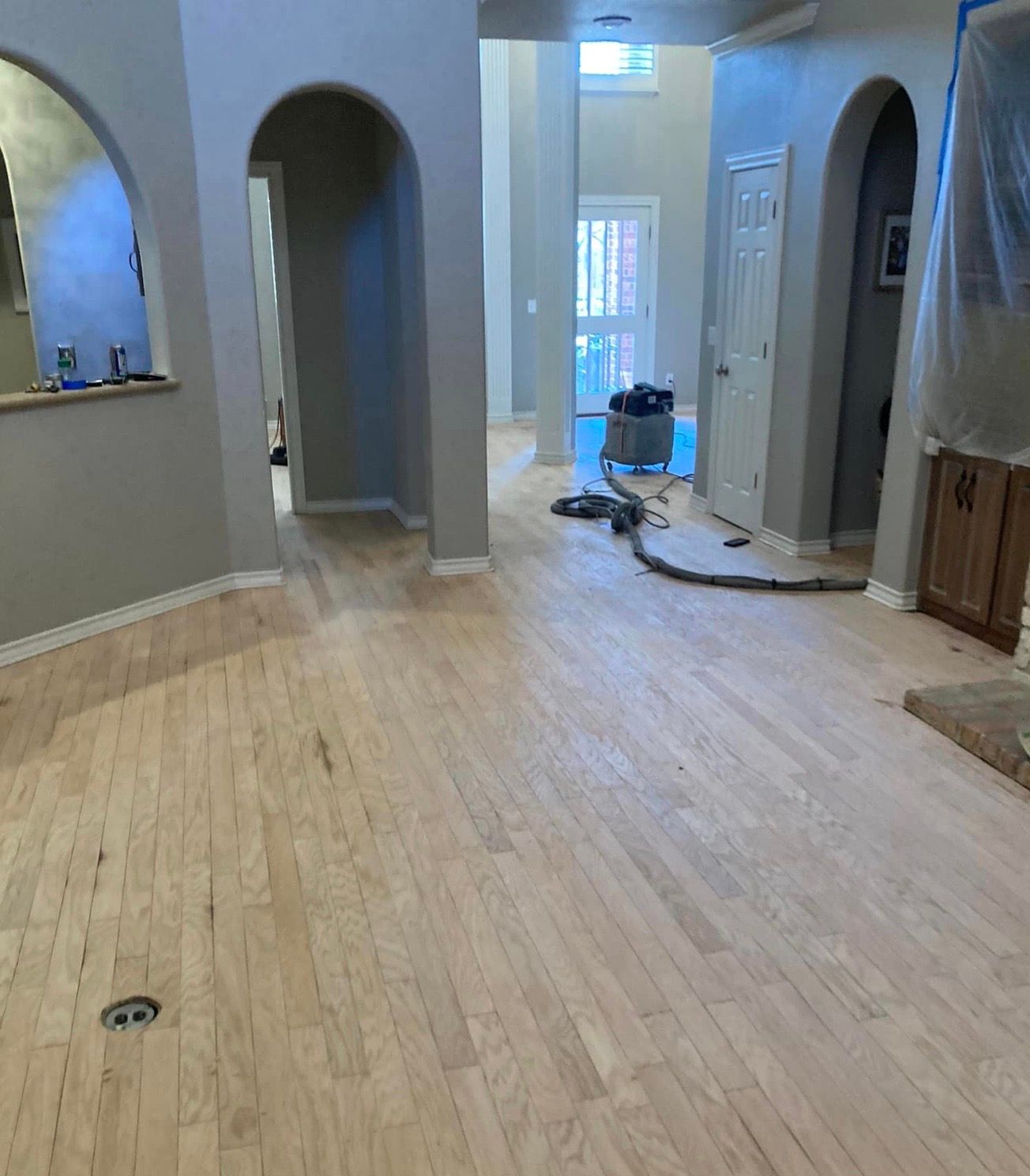 Newly installed light wood floor in a home with arched doorways and grey walls.