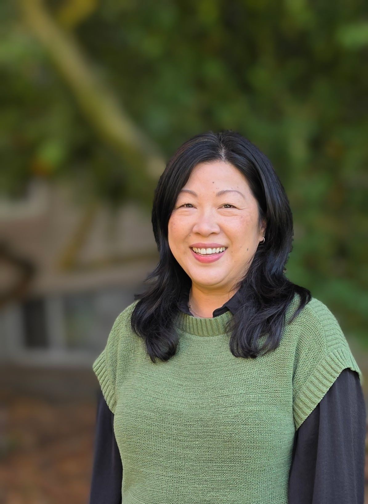 A woman wearing a scarf and a sweater is standing in front of a tree.