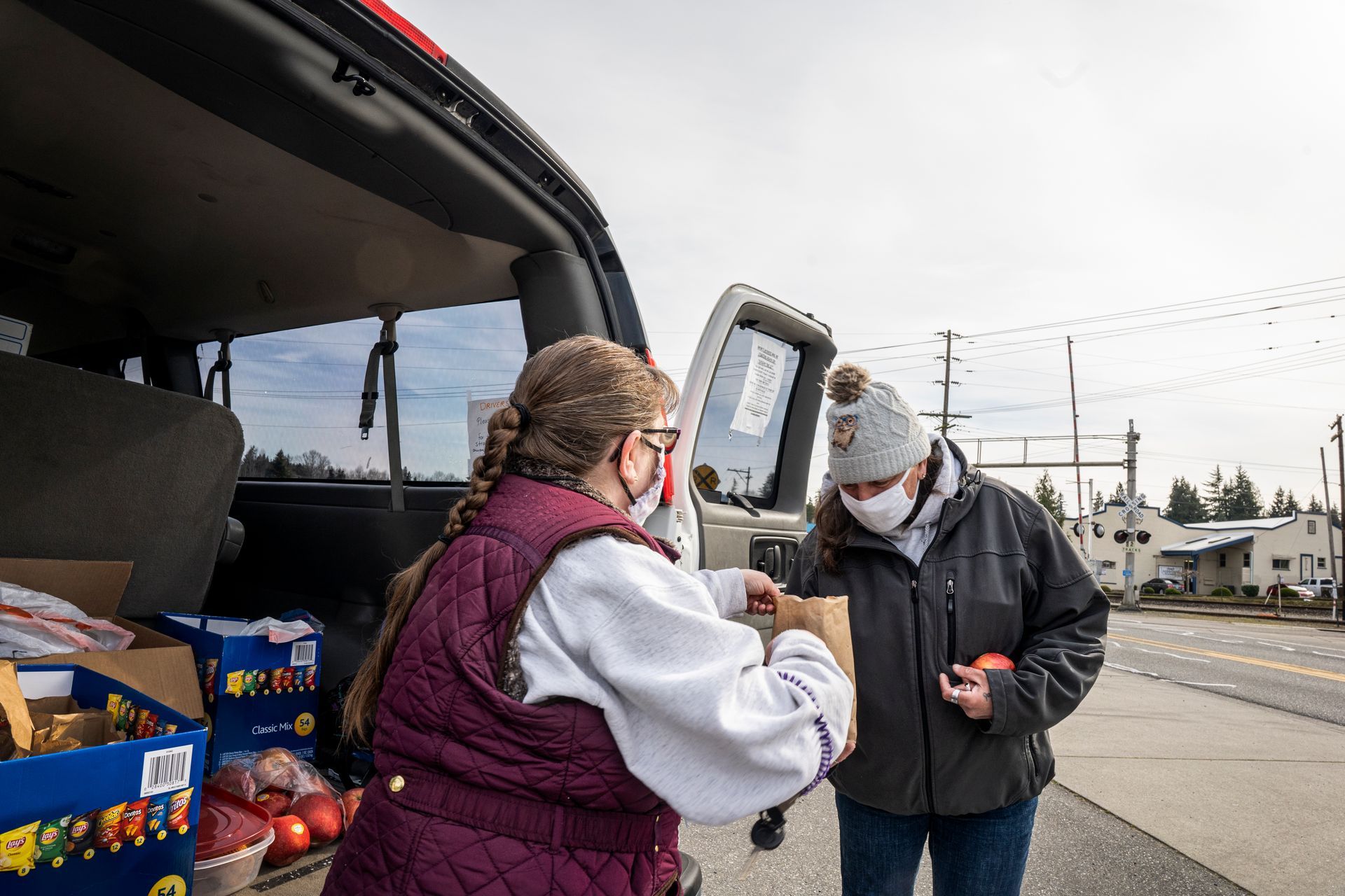 A woman is giving a bag of food to another woman in front of a van.