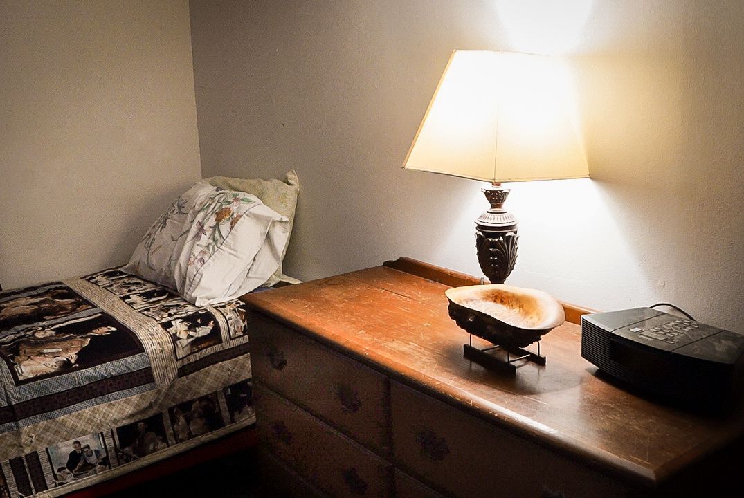 A lamp is sitting on a wooden dresser next to a bed.
