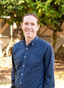 A man in a blue shirt is standing in front of a tree.