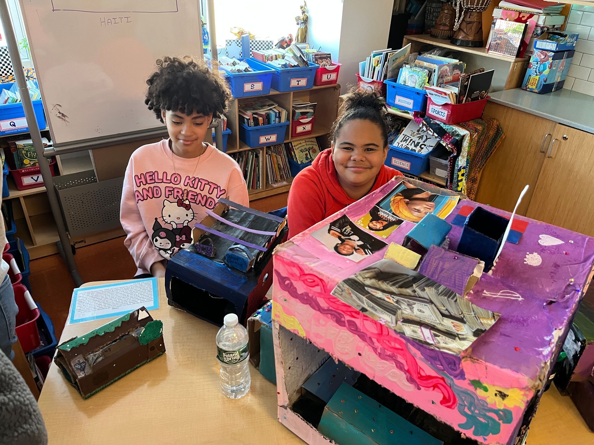 Two girls are sitting at a table with boxes and a water bottle