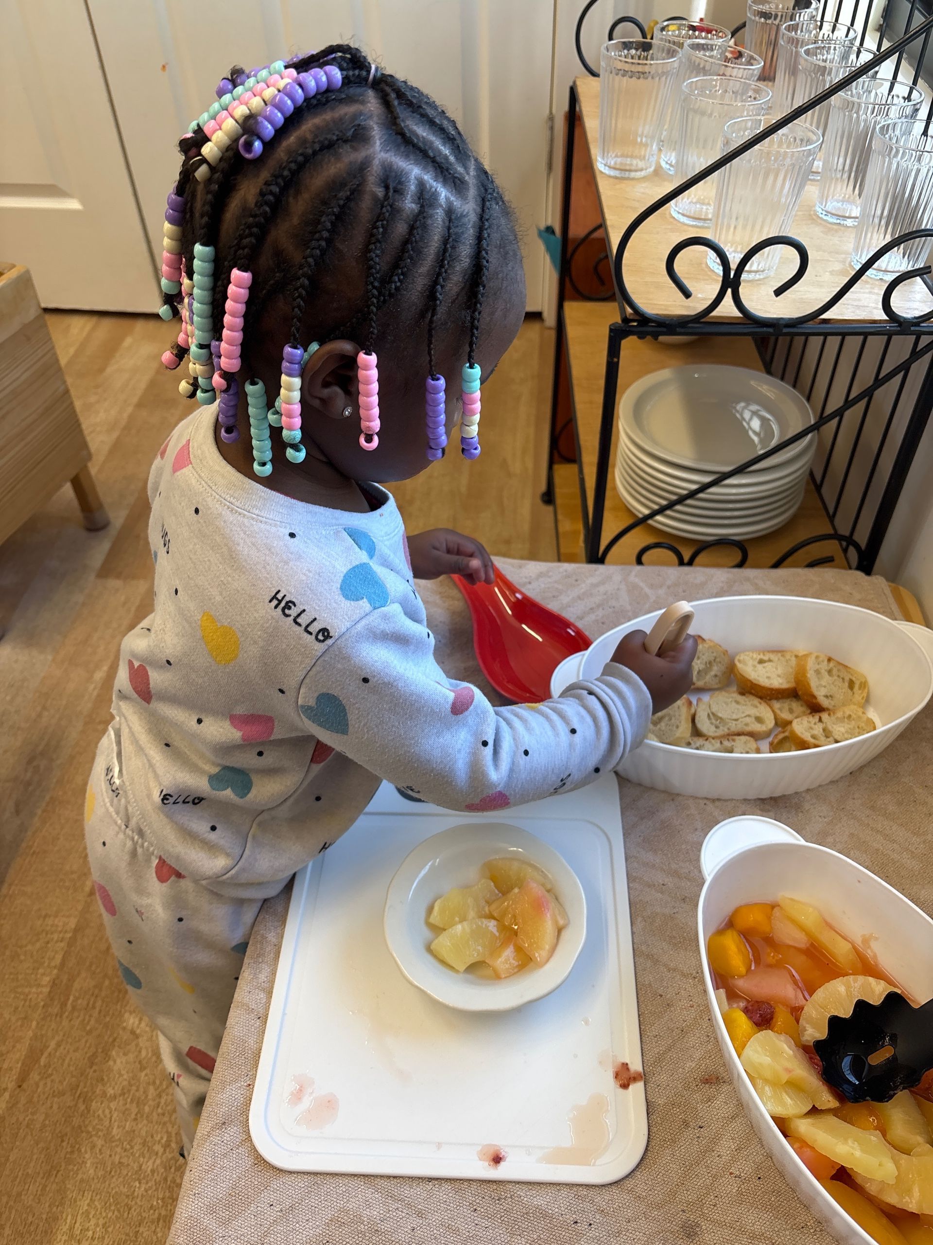 Montessori child serving food at a table with bowls of fruit and crackers.