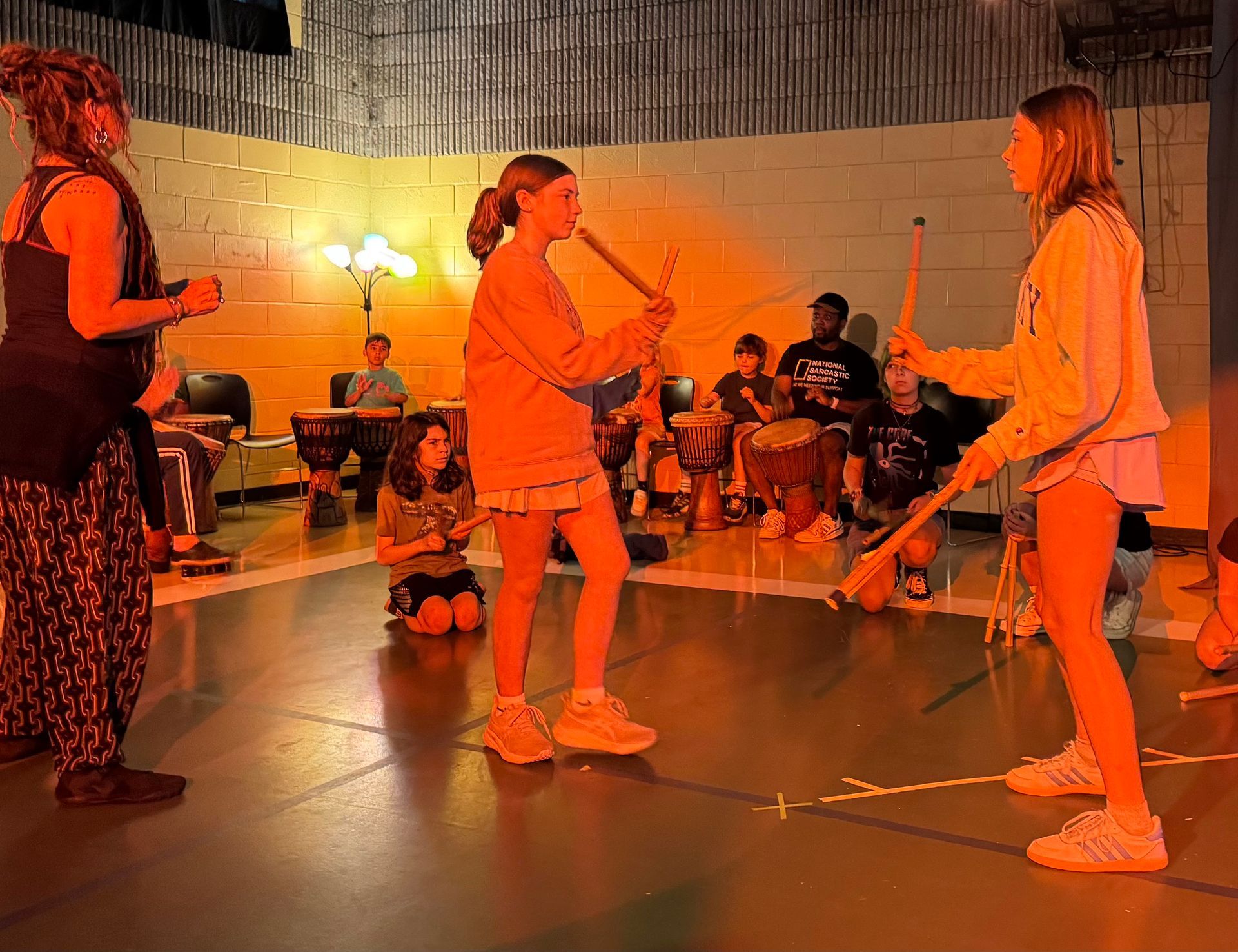 Two people fencing indoors while an audience watches under warm orange lighting