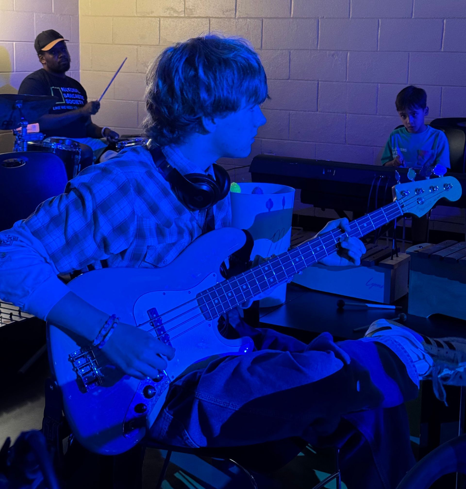 Blue-lit rehearsal scene with a seated guitarist in the foreground and two musicians in the background