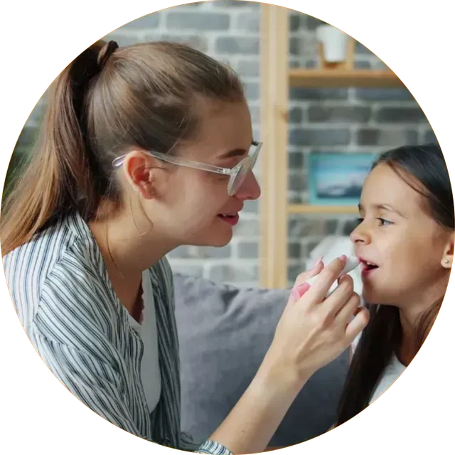 Woman applies lip balm to smiling child indoors