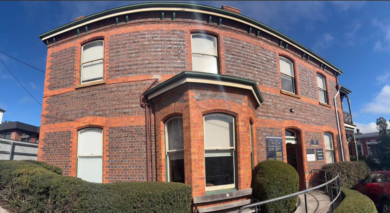 Red brick curved townhouse with white-trimmed windows and a small front entrance under a blue sky