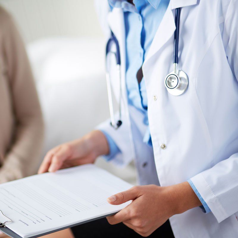 Doctor in white coat holding a clipboard with paperwork and a stethoscope around the neck