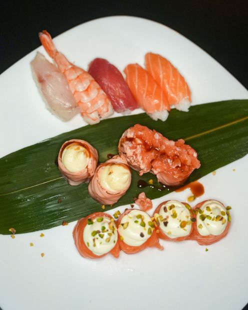 Involtini di sushi con salmone e avocado su un piatto nero, con le bacchette inserite.