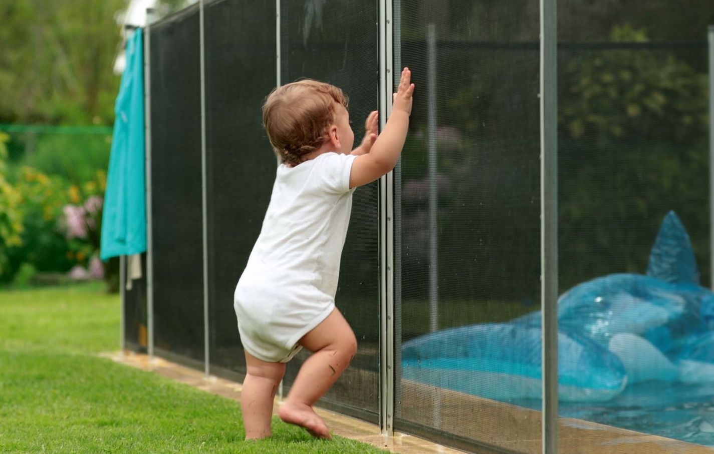 a baby is standing next to a pool fence .