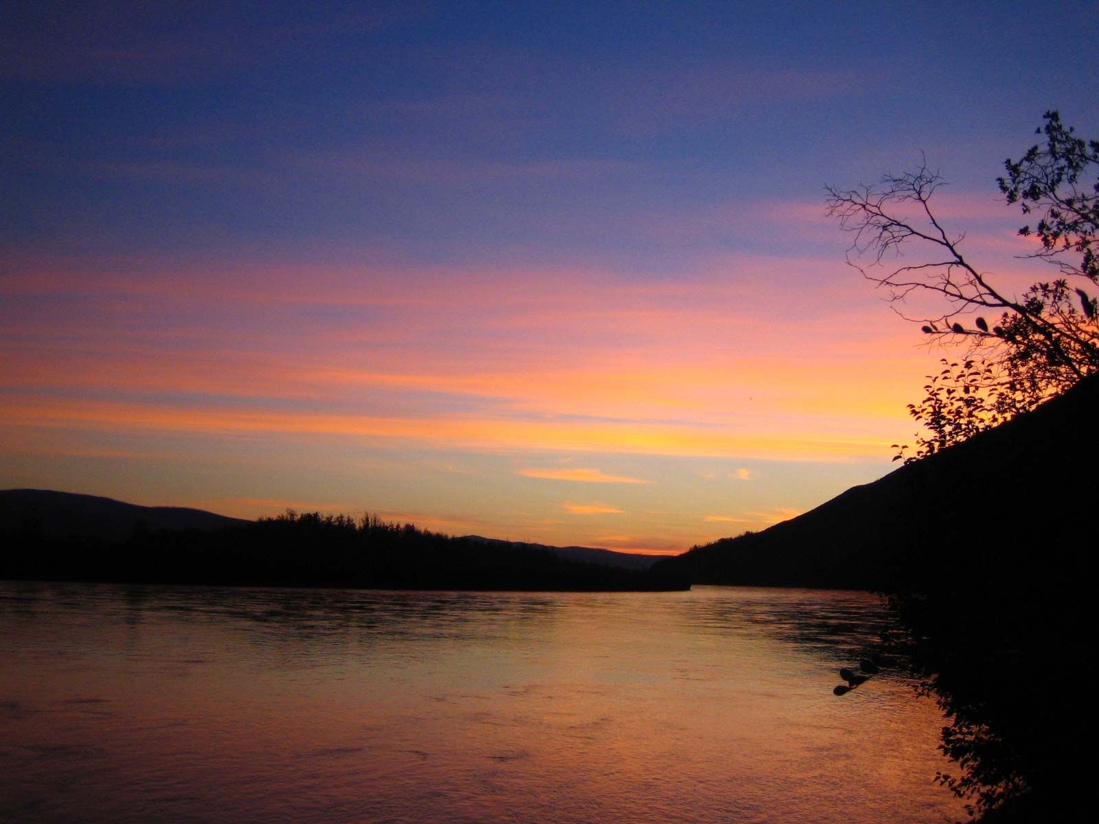 Sunset over a calm lake with pink and orange sky and dark tree-lined shores