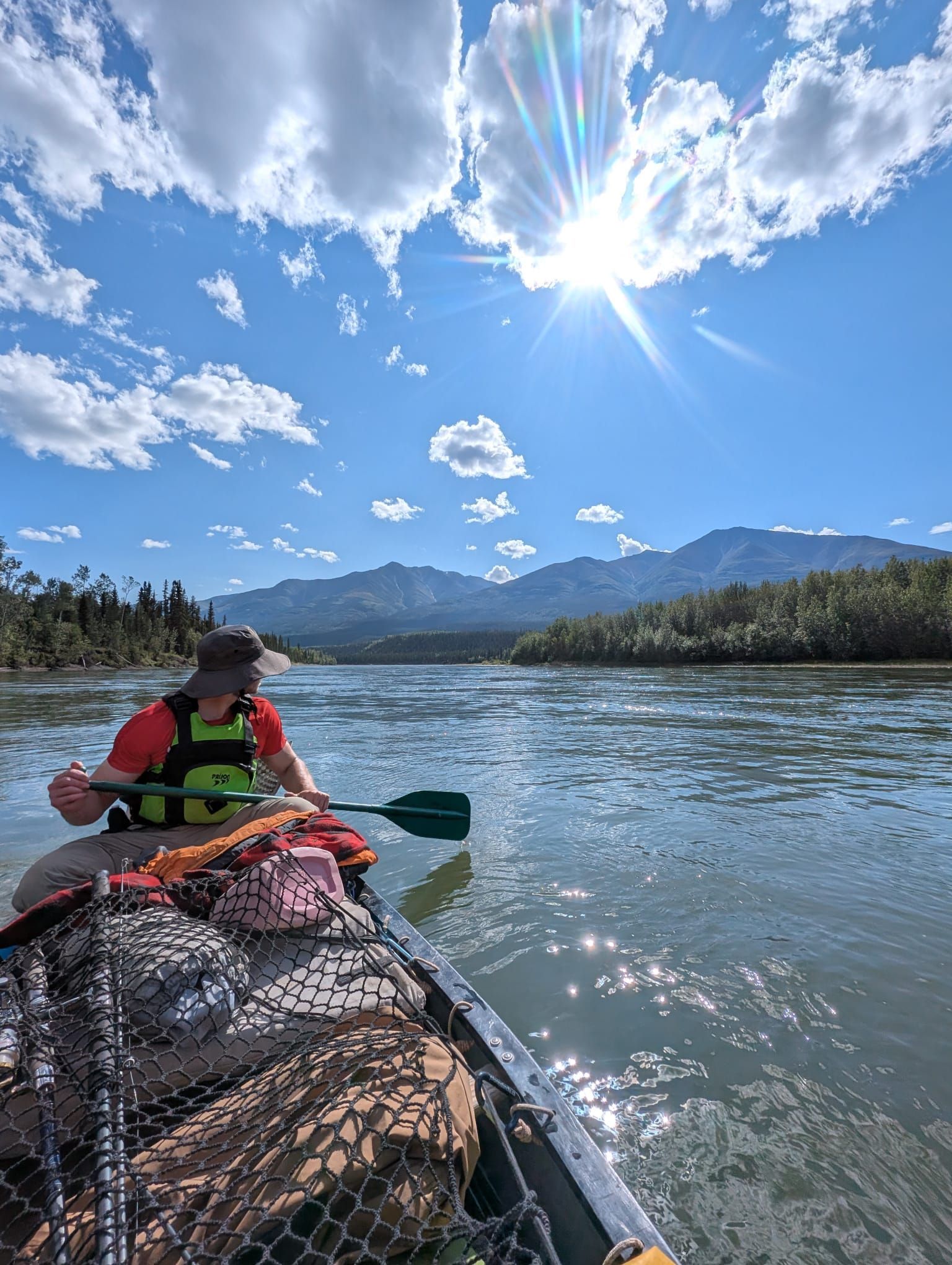 Kayaker in a life jacket paddling on a sunlit lake with mountains and blue sky in the background