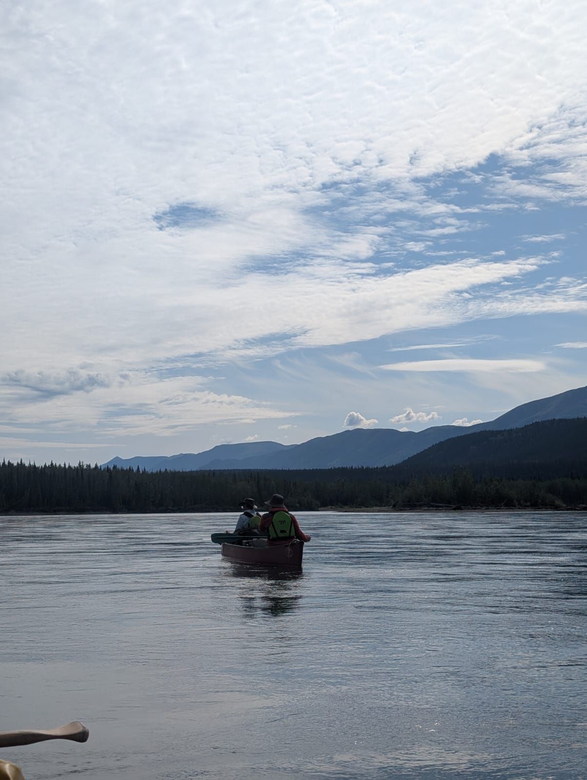 Small boat with people on a calm lake, with mountains and cloudy sky in the background
