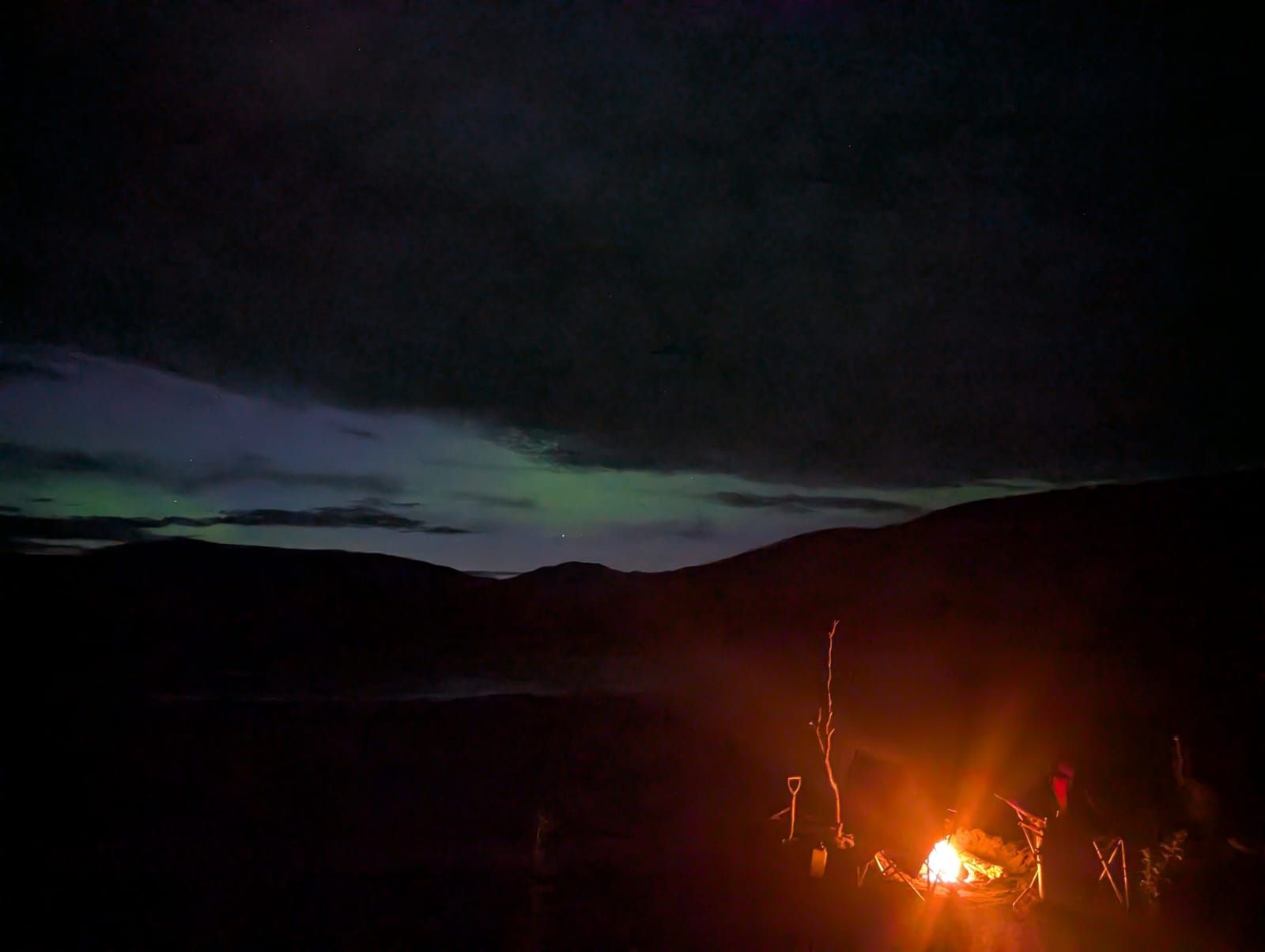 Campfire glowing in a dark campsite beneath a cloudy twilight sky