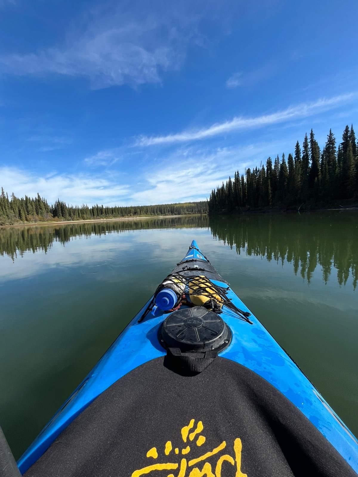 Kayak bow on a calm lake with blue sky and pine forest reflections