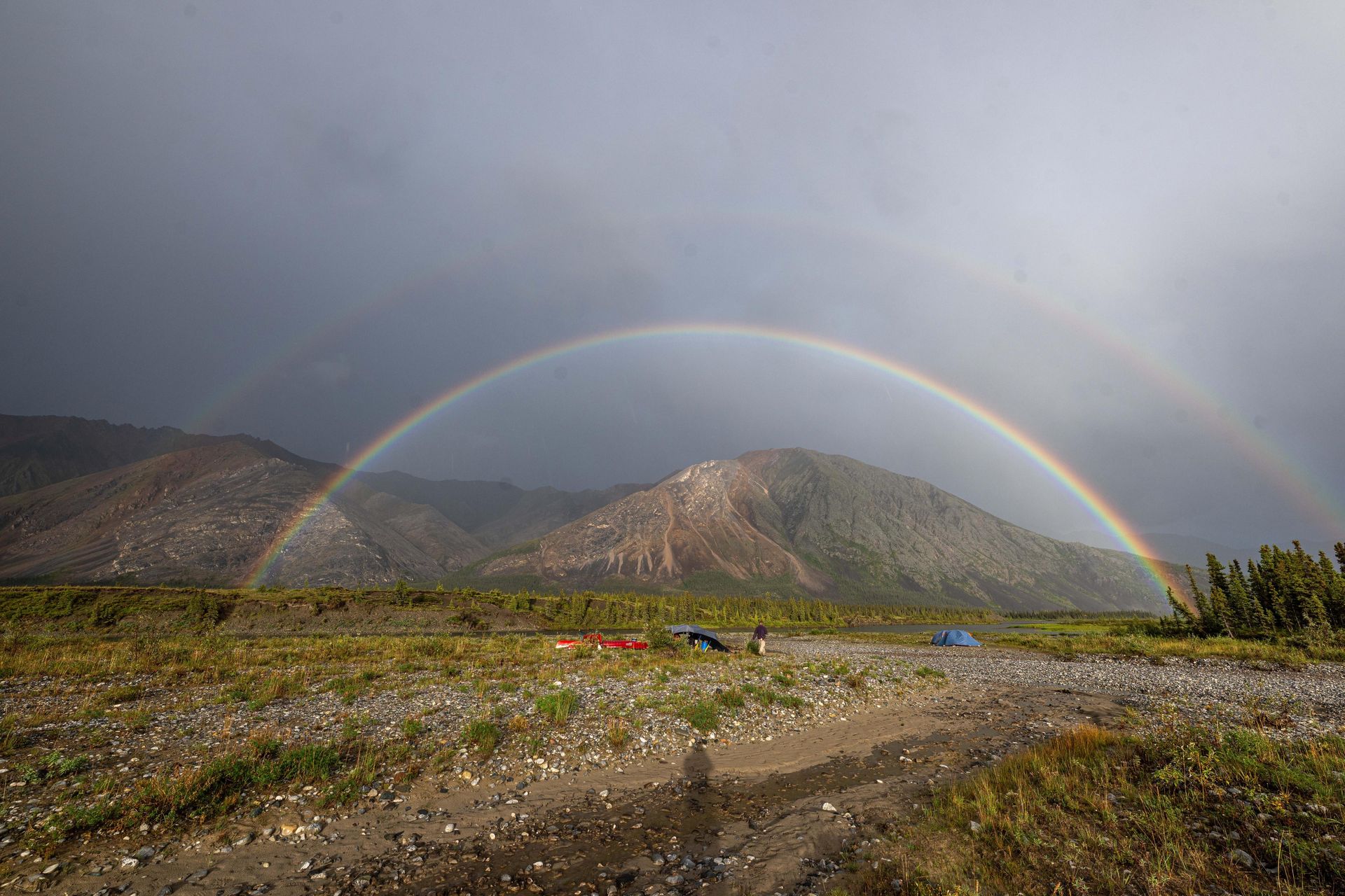 Rainbow over mountains and rocky plain under a cloudy sky