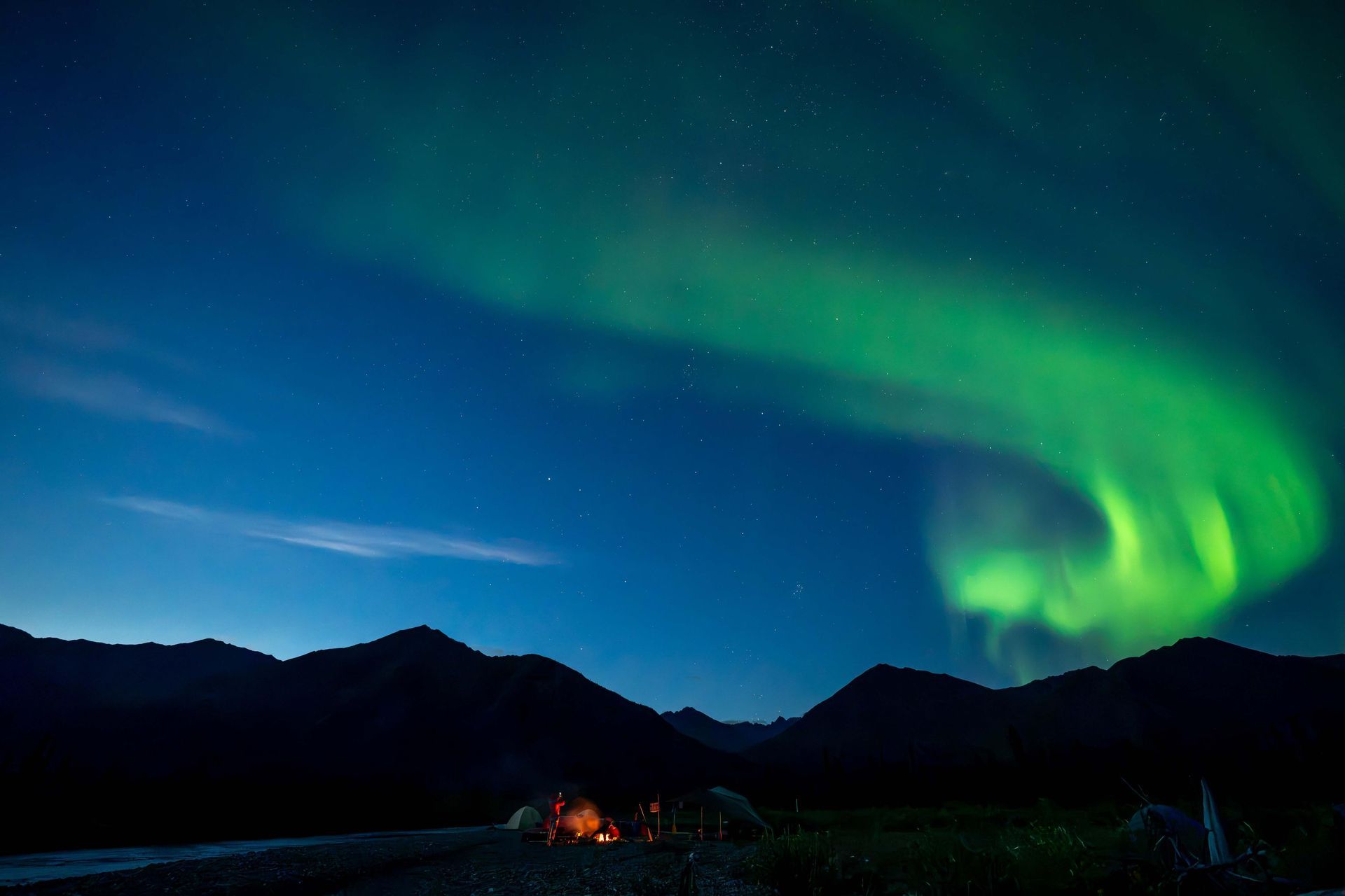 Green aurora over dark mountains and a starry night sky