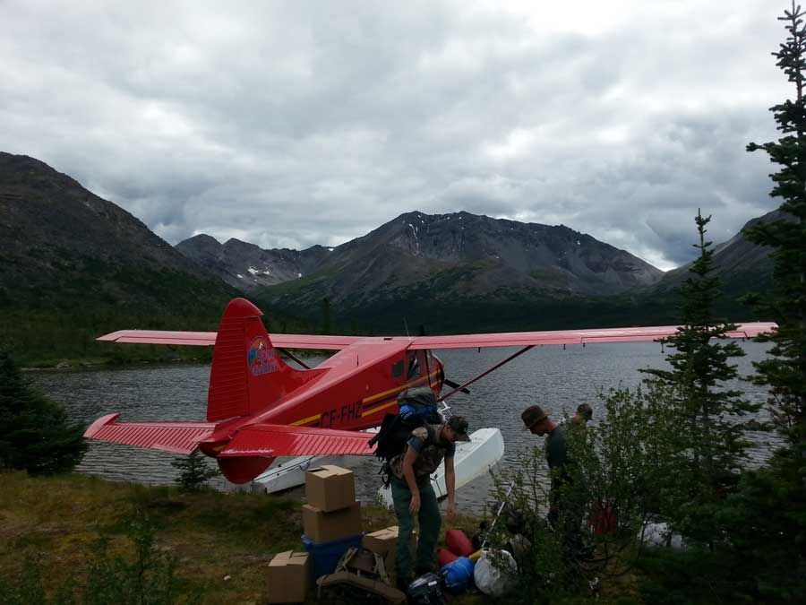 Red floatplane by a mountain lake with people loading gear on the shore