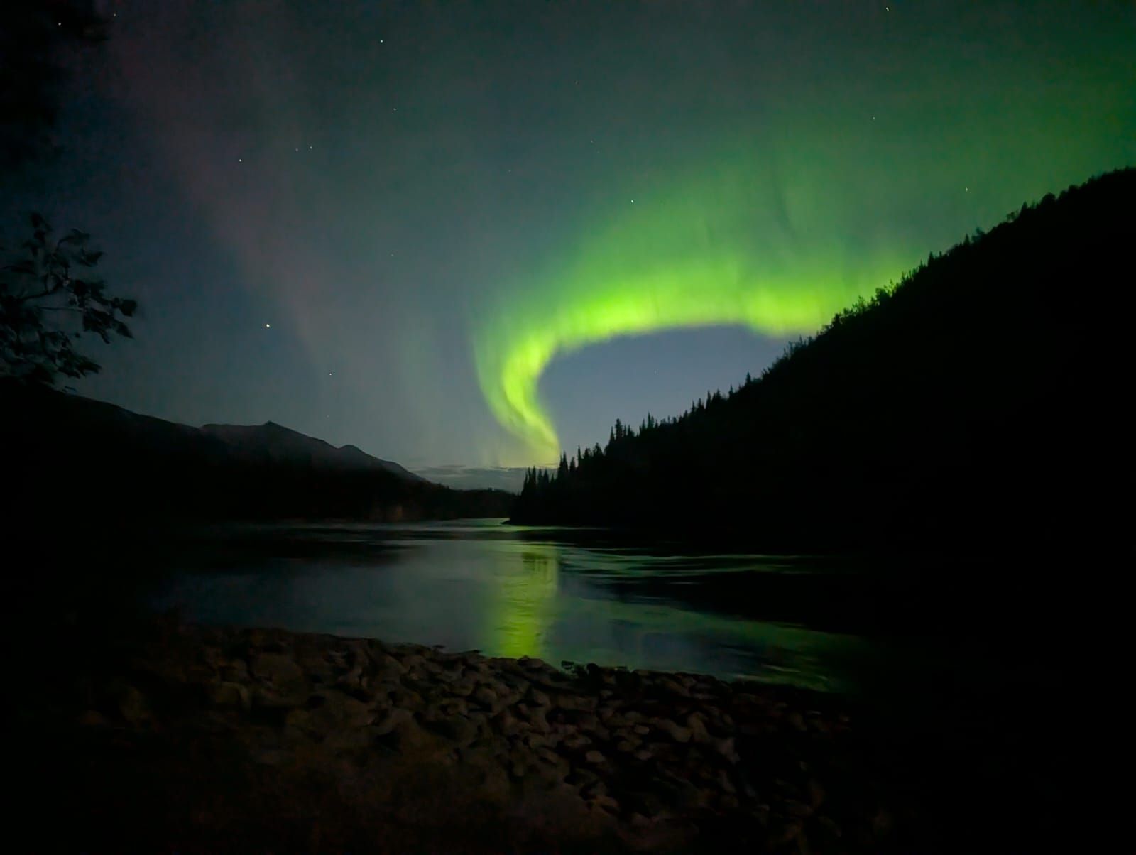 Green aurora over a dark lake between silhouetted mountains at night