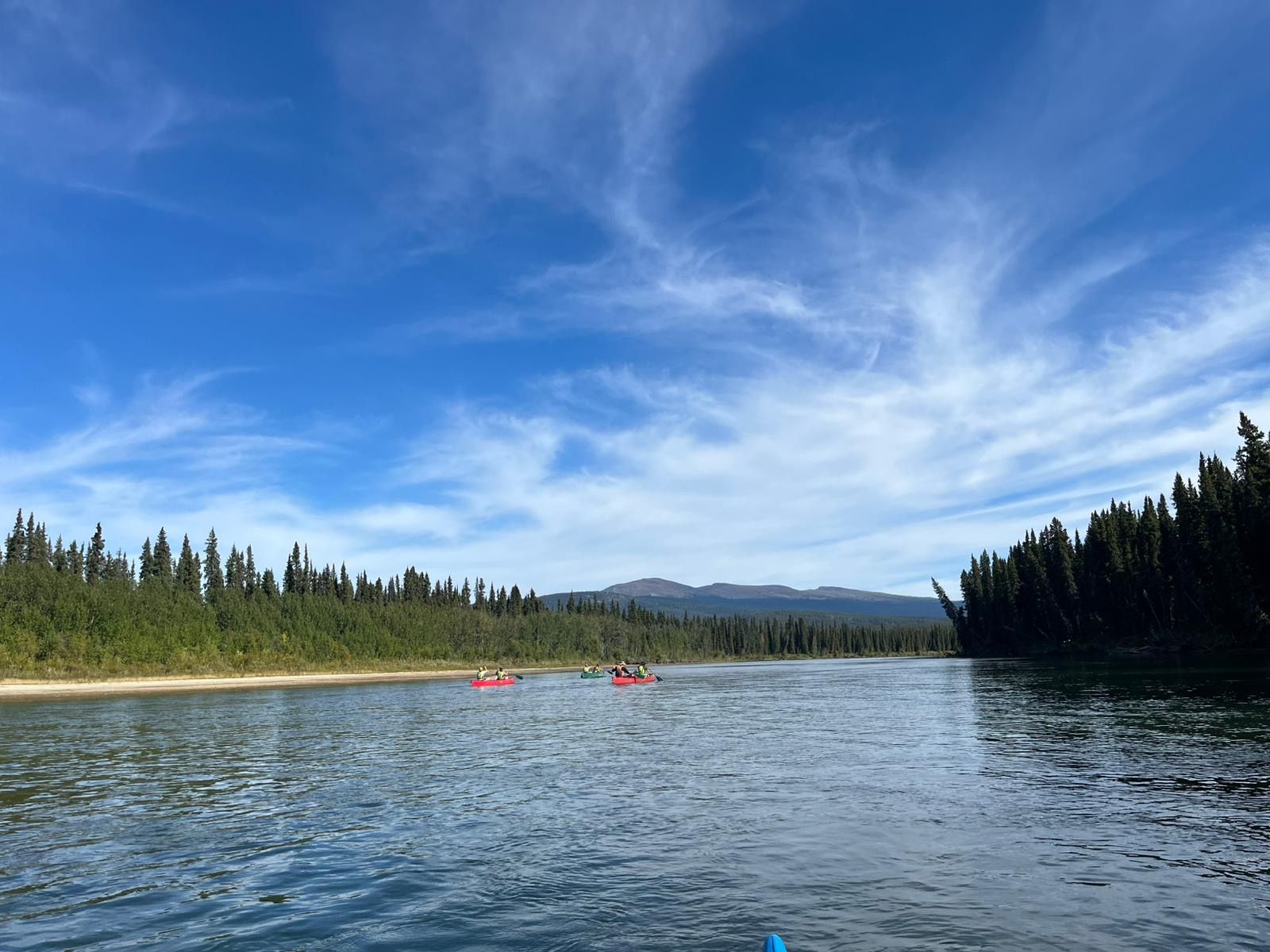Two red kayaks on a calm lake with forested shores and mountains under a blue sky