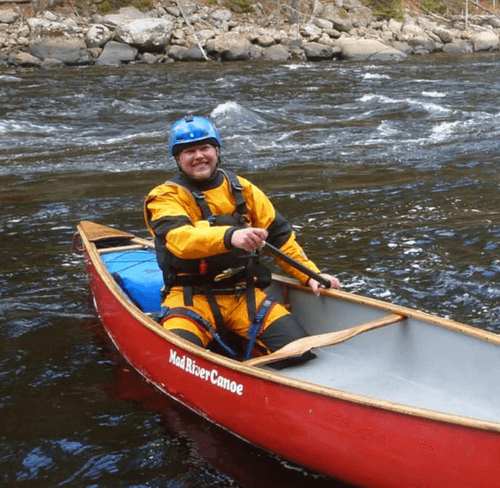 Smiling kayaker in yellow jacket and blue helmet paddling a red canoe on a rocky river