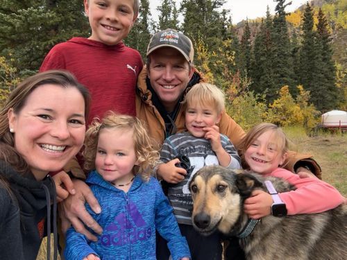 Smiling family with a large dog outdoors in autumn, with trees and a grassy field in the background