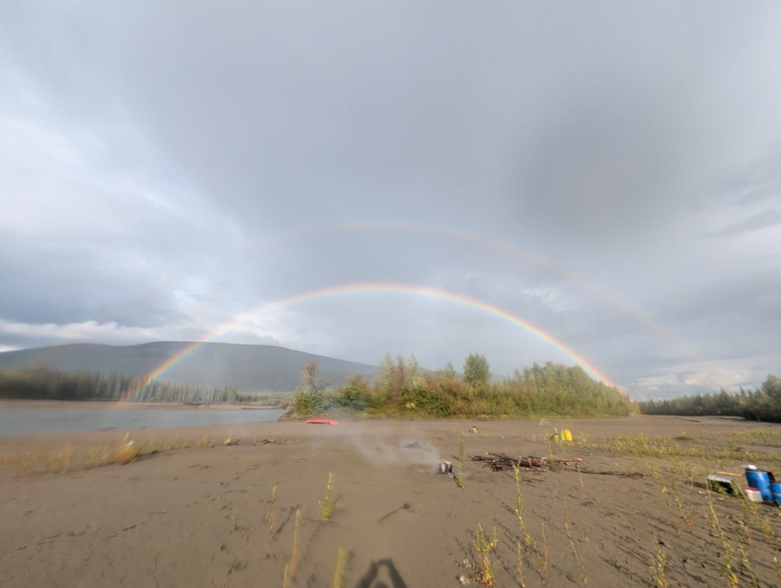 Rainbow over a muddy shoreline with mountains and cloudy sky in the background