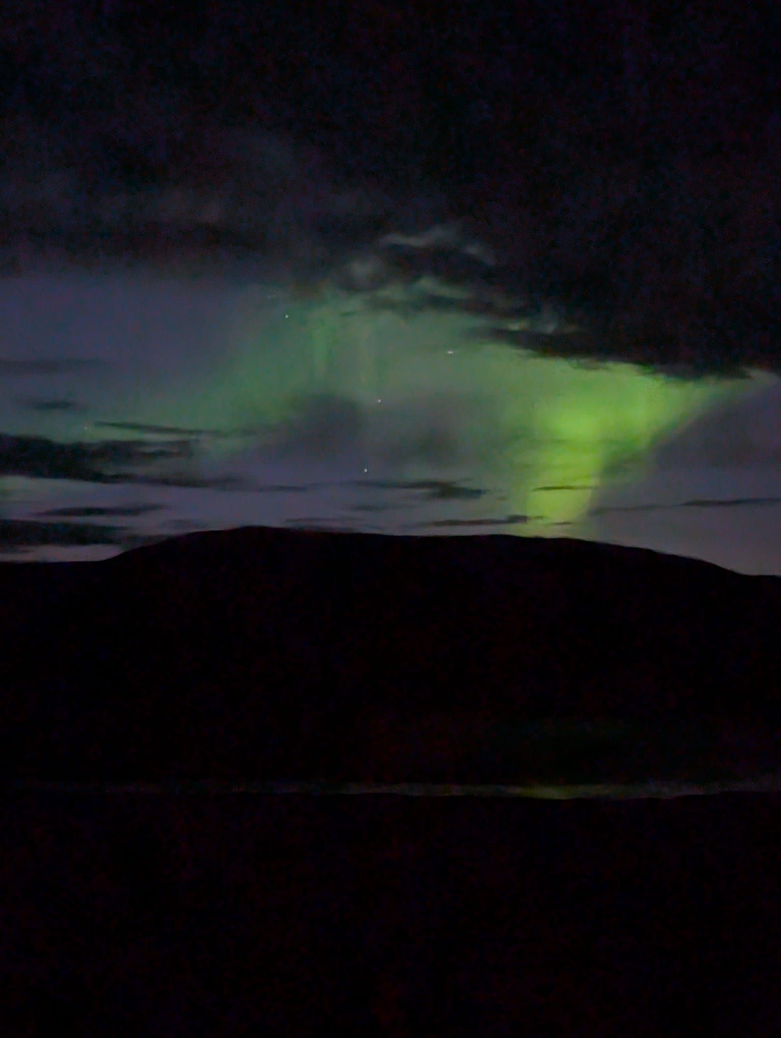 Green aurora glowing over dark hills at night