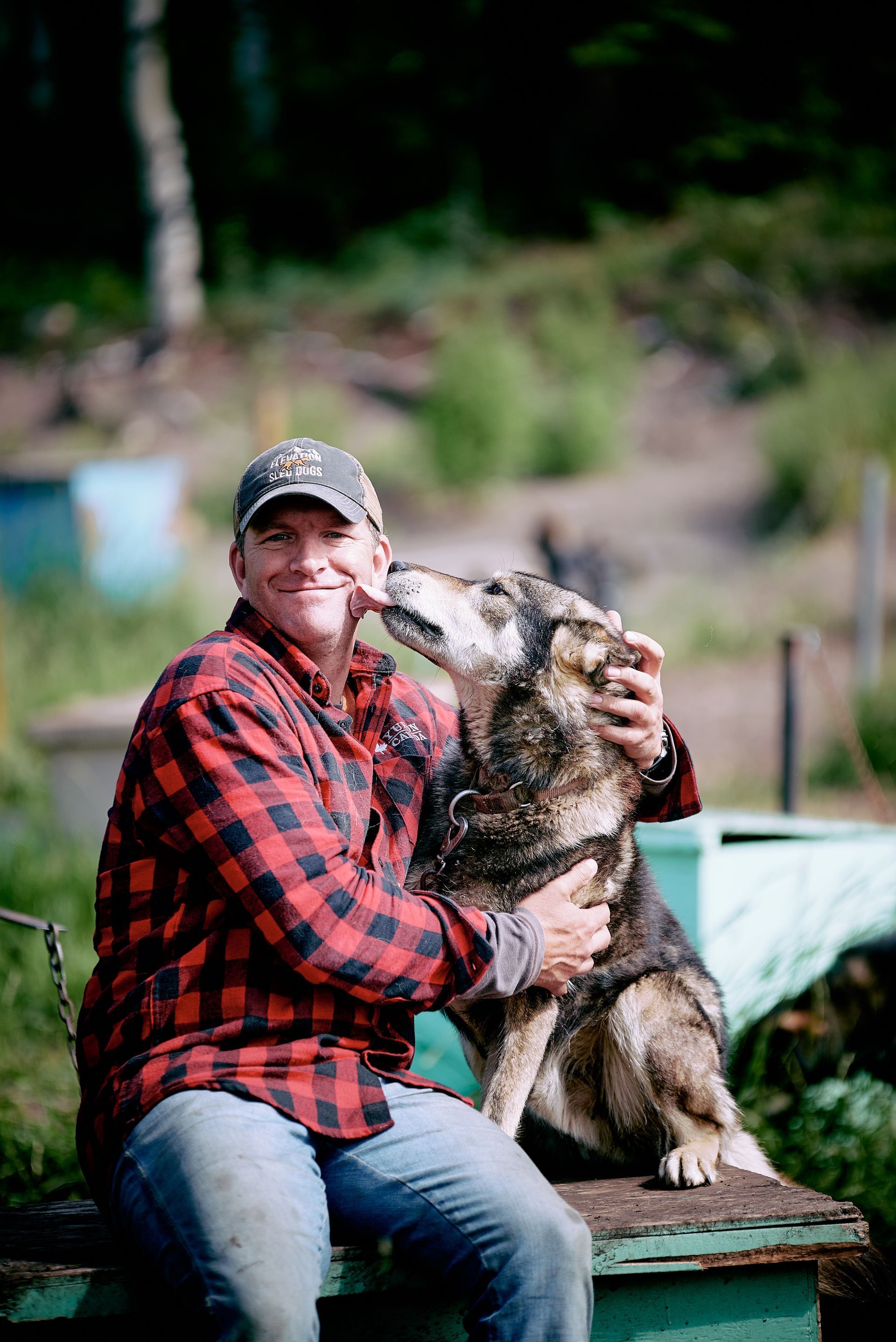 Person in a red plaid shirt holds a large cat in an outdoor setting.
