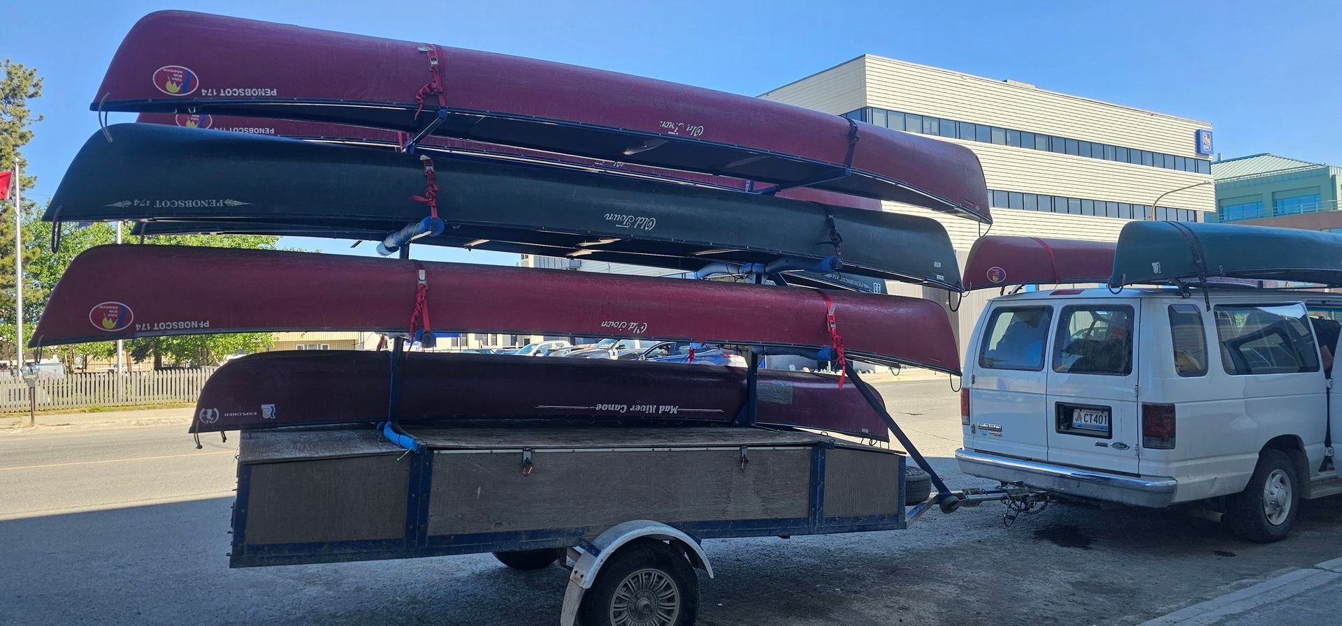 White truck hauling stacked red and dark canoes on a trailer in a parking lot