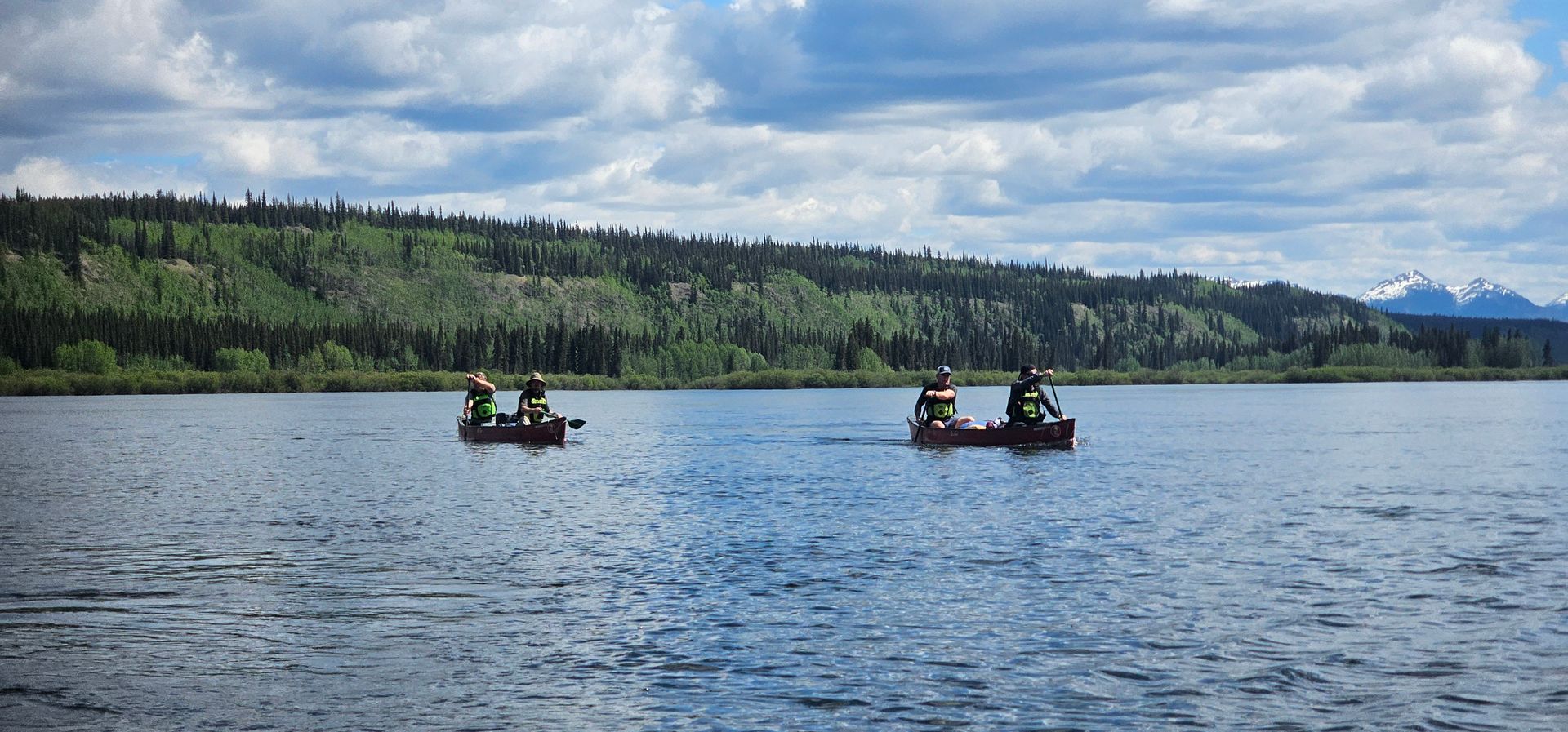 Two rowboats on a blue lake with forested hills and cloudy sky in the background