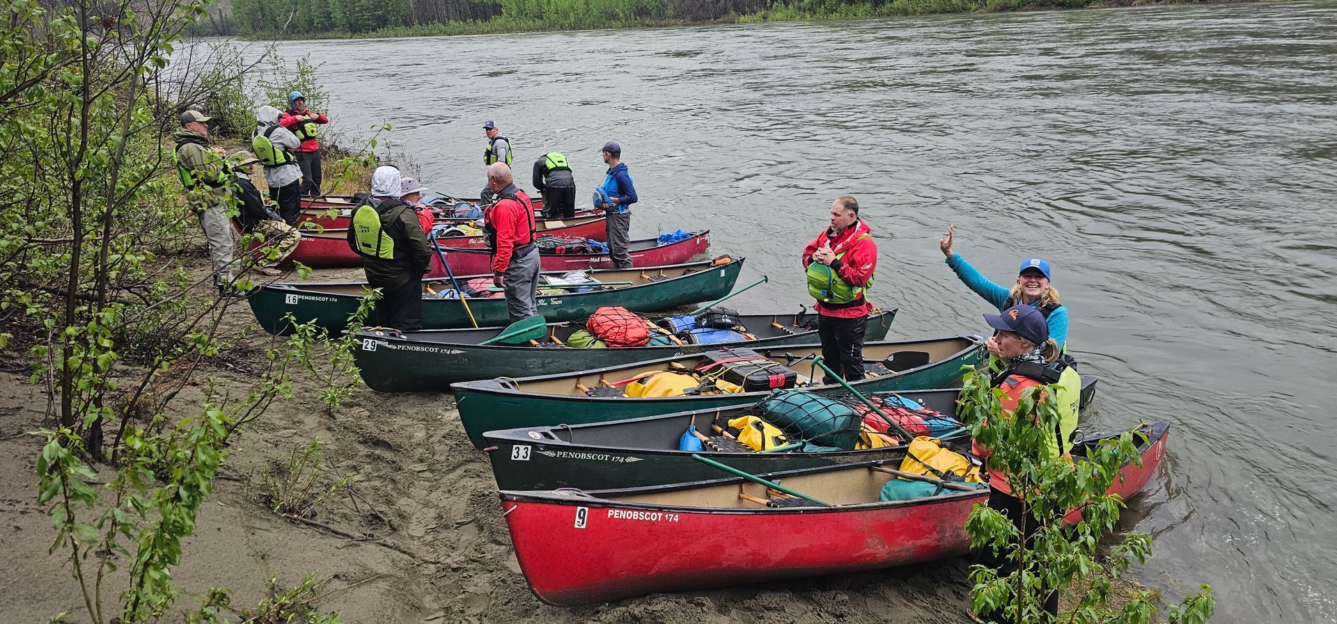 People in bright jackets paddling colorful canoes on a riverbank