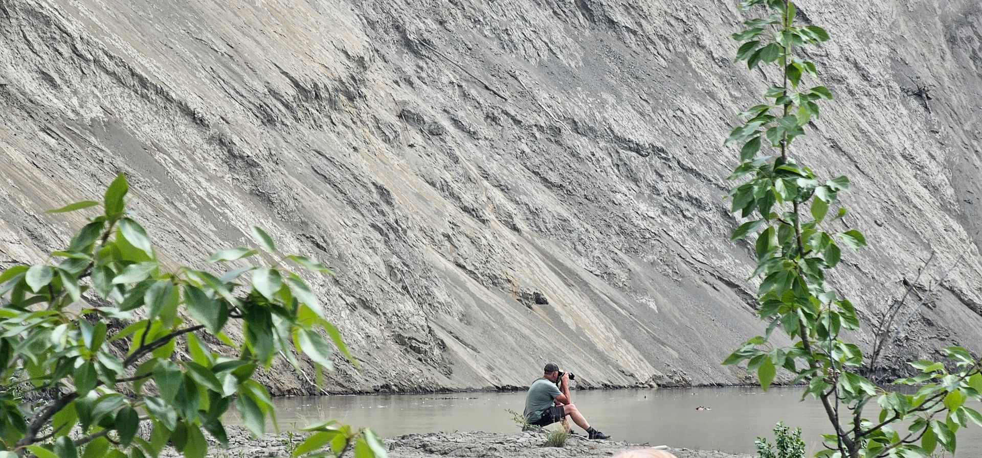 Person in a red kayak paddling on a calm lake beside a steep rocky cliff