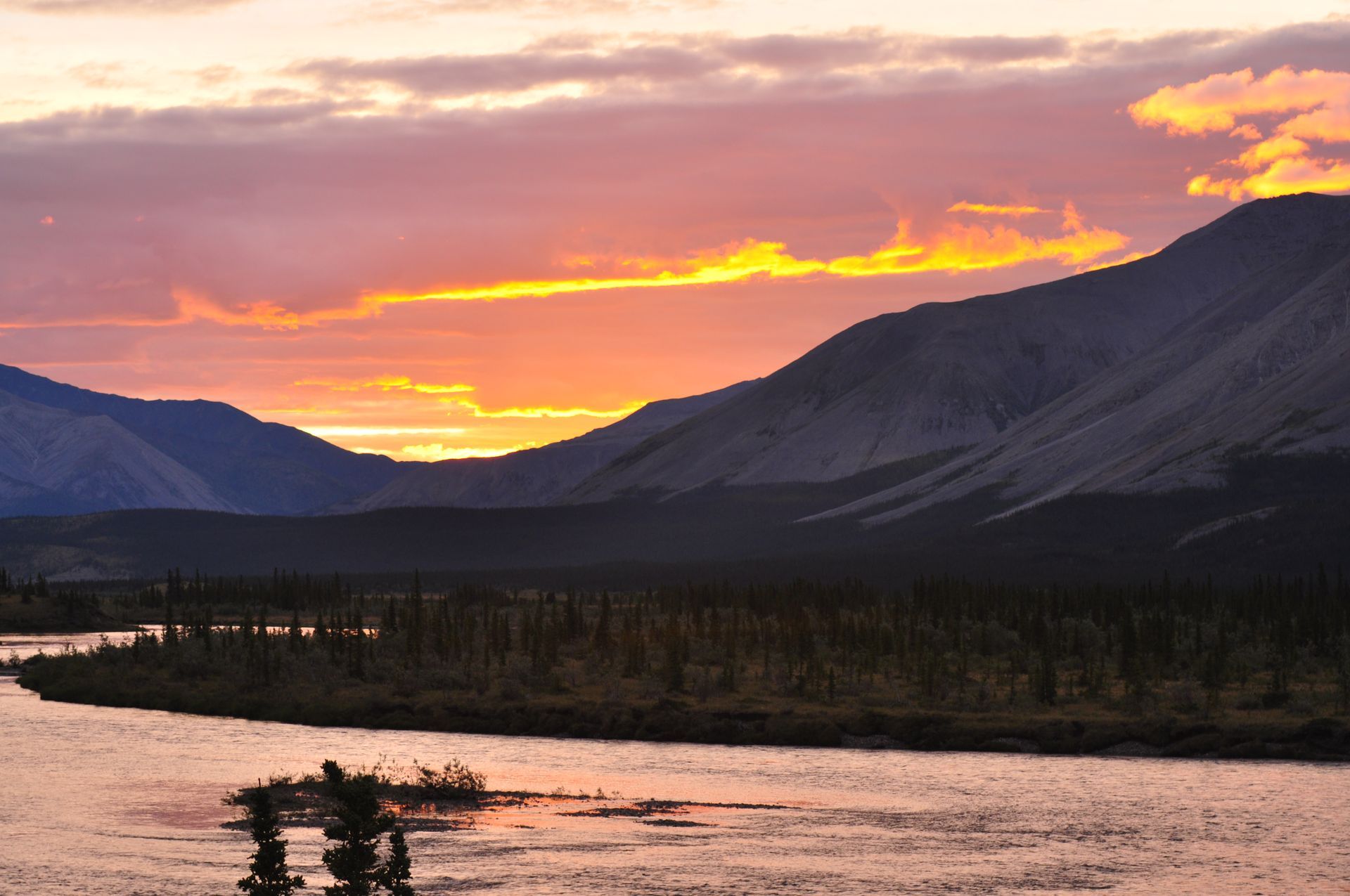 Sunset over a river valley with dark mountains and orange-pink clouds
